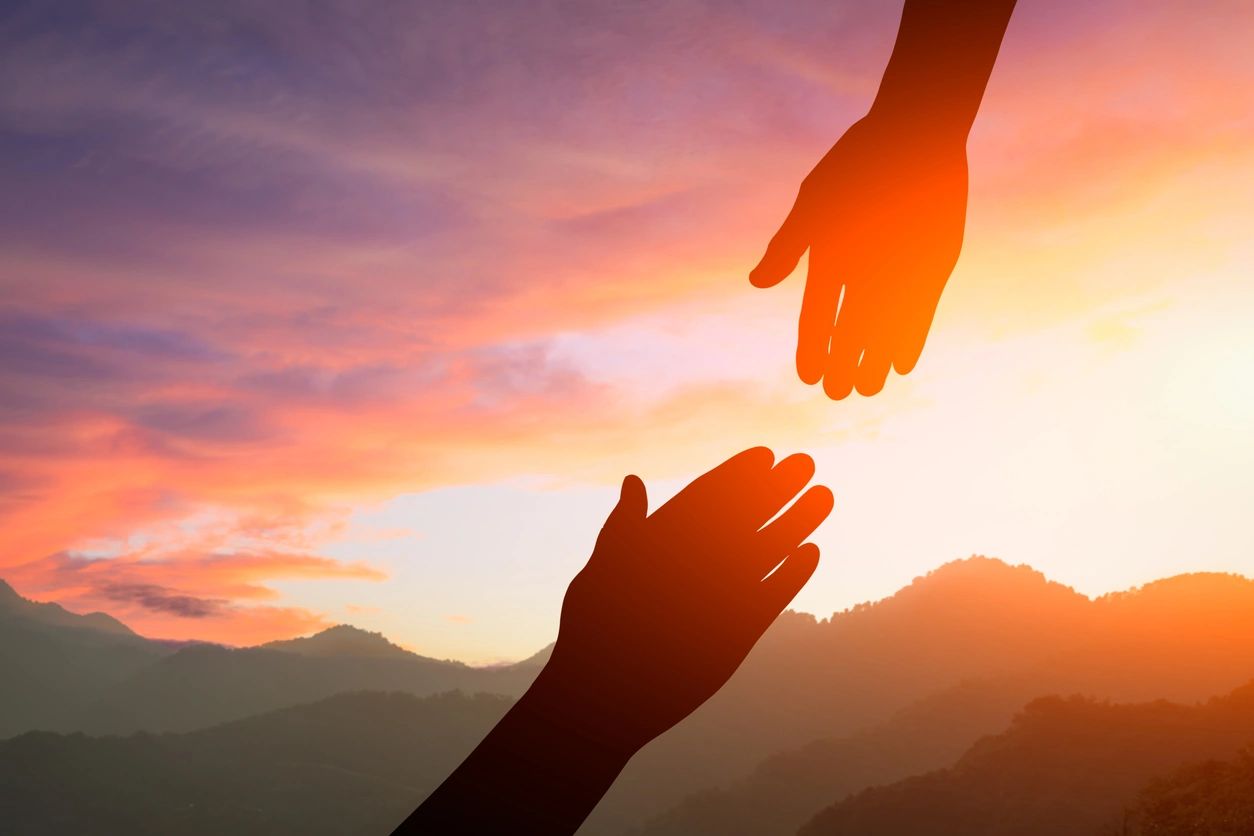 Two hands reaching towards each other against a sunset sky.