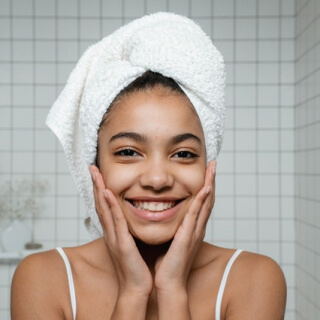 Smiling woman with a towel wrapped around her head in a bathroom.